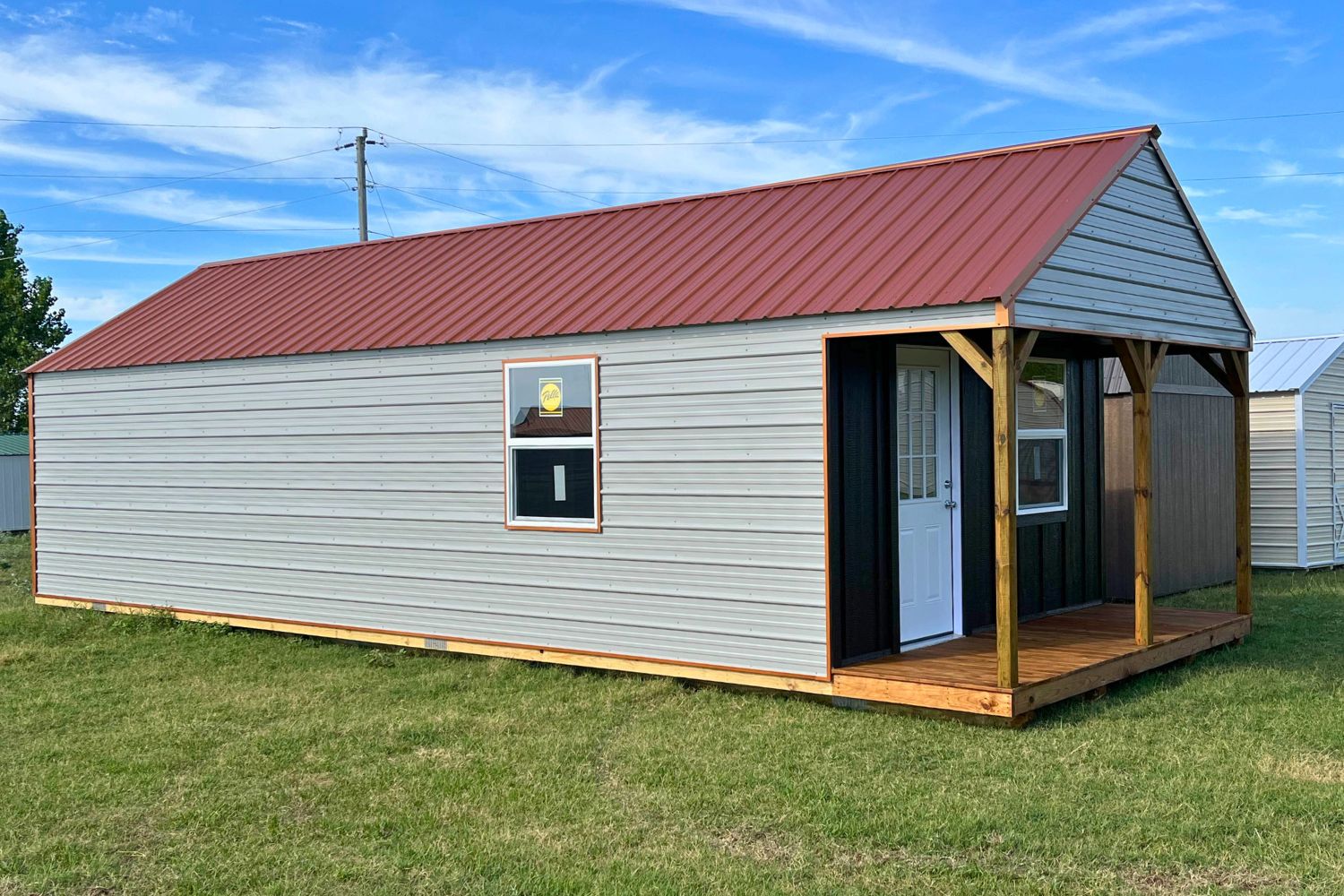 Gray and red portable cabin with a wooden porch, white front door and two single windows