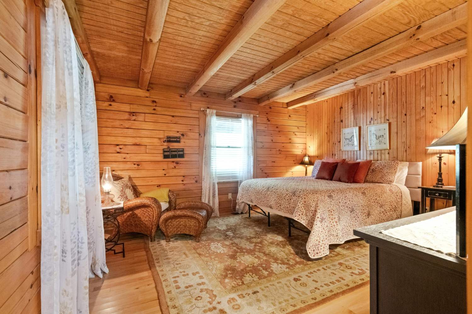 Inside bedroom in log cabin with wooden walls, two windows, large bed and seating area